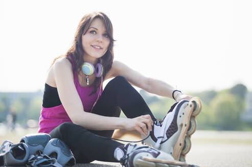 Lächelnde, zuversichtliche junge Frau, die Inline-Skates trägt, während sie gegen den klaren Himmel im Park sitzt - DIGF12391