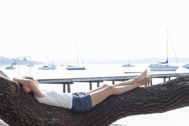 Woman relaxing on tree trunk at Ammersee, Germany - DIGF12412