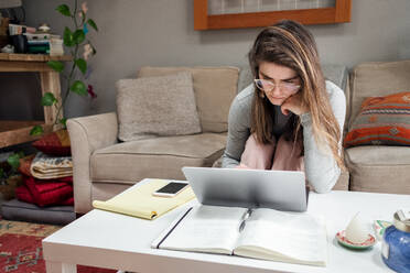 Junge Frau arbeitet während der COVID von zu Hause aus am Laptop - CAVF83006