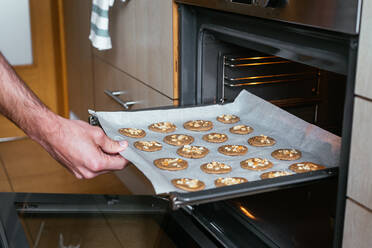 Young man putting the home-made cookies in the oven - CAVF83019