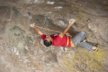 One man wearing red clips a carabiner with a rope while rock climbing - CAVF83040