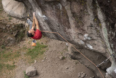 Ein Mann in Rot hält sich beim Klettern mit beiden Händen an einer Felswand fest - CAVF83044