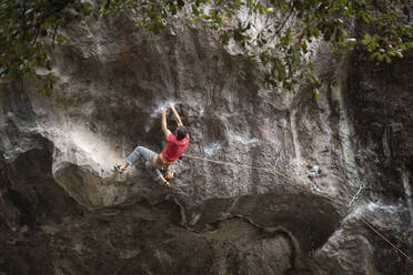 One man wearing red holds with both hands on rock wall while climbing - CAVF83045