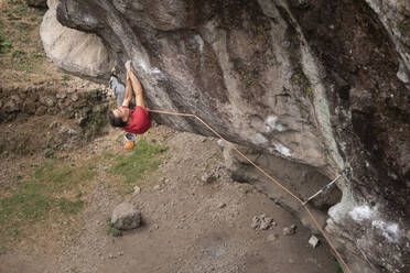 One man wearing red holds with both hands on rock wall while climbing - CAVF83052