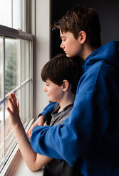 Zwei Jungen, die gemeinsam mit traurigen Gesichtern aus dem Fenster schauen. - CAVF83053