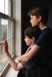Zwei Jungen, die gemeinsam mit traurigen Gesichtern aus dem Fenster schauen. - CAVF83054