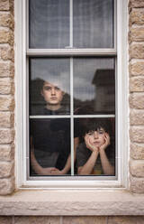 Zwei Jungen, die gemeinsam mit gelangweilten Gesichtern aus dem Fenster schauen. - CAVF83057