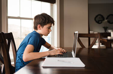 Tween boy working on his homework on a laptop commuter at home. - CAVF83078