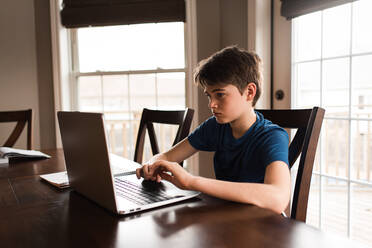 Tween boy working on his homework on a laptop commuter at home. - CAVF83079