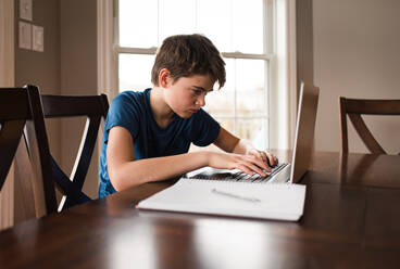 Tween boy working on his homework on a laptop commuter at home. - CAVF83080