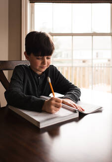 Young boy doing schoolwork in a workbook at home at the table. - CAVF83082