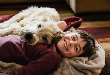 Boy and his dog cuddling on the floor together on a blanket. - CAVF83085