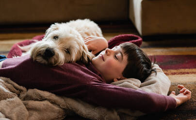 Boy and his dog cuddling on the floor together on a blanket. - CAVF83087