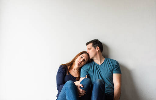 Ausgeschnittenes Bild eines liebenden Paares, das zusammen vor einer weißen Wand sitzt. - CAVF83088