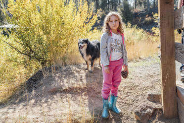 Mädchen mit Tannenzapfen auf einem Feld im Herbst mit Hund - CAVF83132