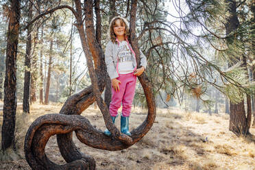 Lächelndes Mädchen in Jogginghose und Gummibüchern auf einem Baumzweig stehend - CAVF83133