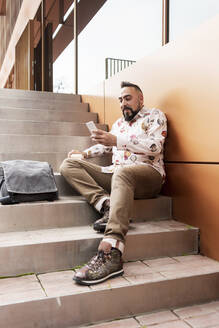 Gut aussehender junger Mann in legerer Kleidung, der seine Zeit im Freien mit dem Handy verbringt - CAVF83163