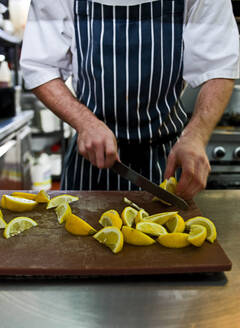 Koch schneidet frische Zitrone in einem Restaurant im Vereinigten Königreich - CAVF83190