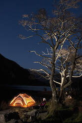 Female hiker sitting outside her tent at camp in North Wales - CAVF83221