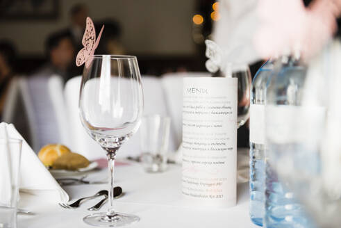 Nahaufnahme eines Weinglases mit Schmetterlingsdekoration und Menü auf einem Tisch bei einem Hochzeitsempfang - DIGF12439