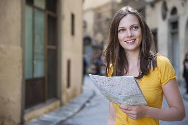 Porträt einer lächelnden Frau mit Stadtplan in einer Gasse, Florenz, Italien - DIGF12445