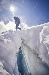 Female mountaineer at crevasse against the sun, Glacier Grossvendediger, Tyrol, Austria - PNEF02598