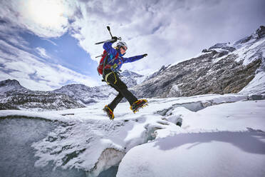 Female mountaineer jumping over crevasse, Glacier Grossvendediger, Tyrol, Austria - PNEF02607