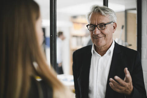 Junge Frau im Gespräch mit einem älteren Geschäftsmann im Büro, lizenzfreies Stockfoto