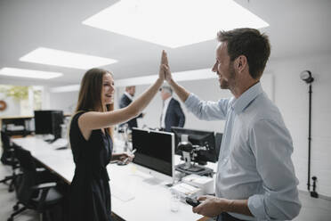 Businesswoman and man highfiving in office, laughing - GUSF03885