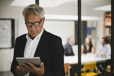 Älterer Geschäftsmann mit digitalem Tablet, Mitarbeiter arbeiten im Hintergrund - GUSF03898