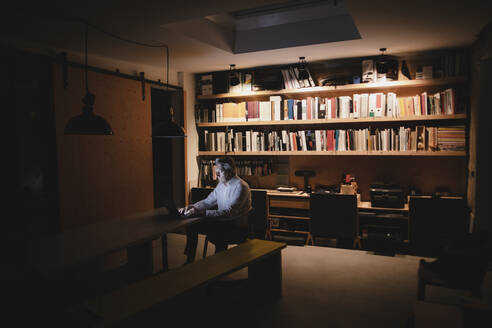 Senior businessman sitting in office, working late - GUSF03914
