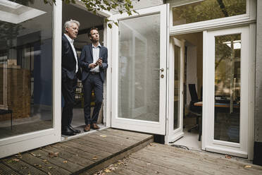 Two businessmen leaning in office door, talking - GUSF03918