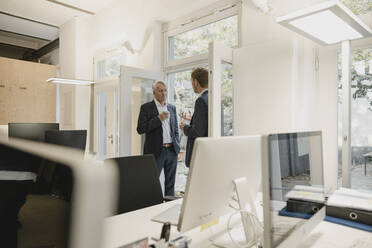 two businessmen standing in office, drinking coffee, talking - GUSF03922