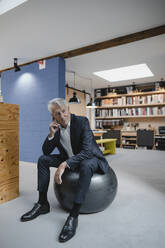 Senior businessman sitting on fitness ball, thinking - GUSF03930