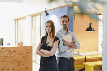 Businessman and businesswoman standing in modern office with arms crossed - GUSF03949