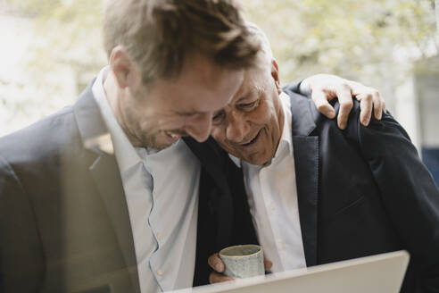 Father leaning on shoulder of his son, looking at laptop, smiling - GUSF03982