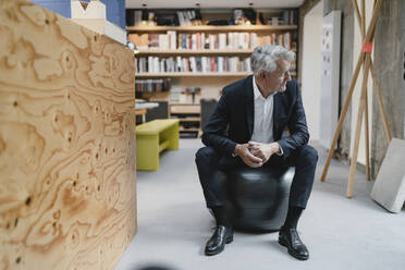 Senior businessman sitting on fitness ball, looking away, smiling - GUSF03984