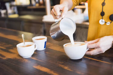 Weiblicher Barista bereitet Cappuccino am Holztisch in einem Café zu - DIGF12454
