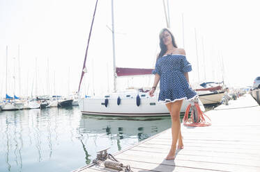 Young woman wearing dress walking on jetty against clear sky during sunny day - DIGF12459