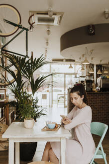 Frau sitzt in einem Café und benutzt ein Mobiltelefon - GMLF00233