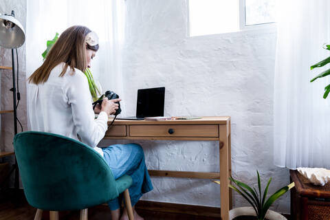 Female photographer using camera while sitting at desk stock photo