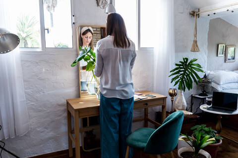 Woman arranging plants in vase while standing at home stock photo