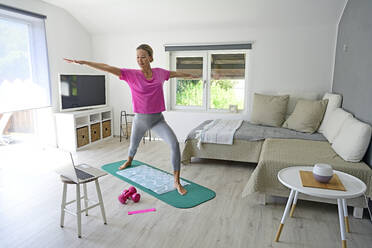 Reife Frau mit Laptop übt Yoga auf Turnmatte im Wohnzimmer - ECPF00920