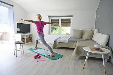 Mature woman with laptop practicing yoga on gym mat in living room - ECPF00923