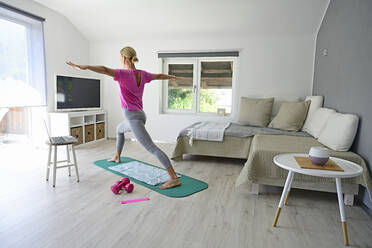 Reife Frau mit Laptop übt Yoga auf Turnmatte im Wohnzimmer - ECPF00923