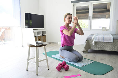 Reife Frau mit Laptop übt Yoga auf Turnmatte im Wohnzimmer - ECPF00926