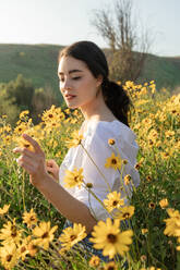 Hübsche Brünette hält Blume in gelben Blumenfeldern und Sonnenschein - CAVF83249