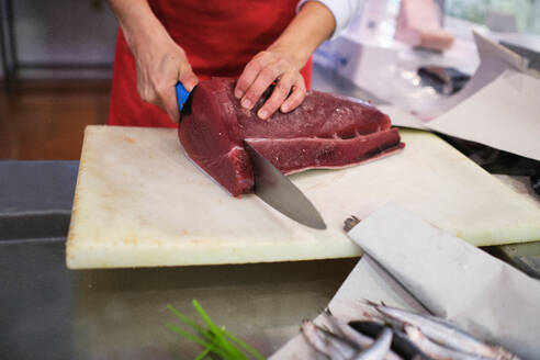 Junge Frau schneidet einen roten Fisch in ihrem Fischgeschäft auf - CAVF83269