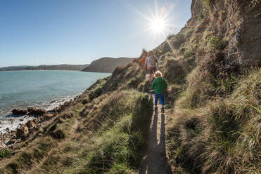 Vater und Kinder wandern auf einem Bergpfad an der Küste in Neuseeland - CAVF83296