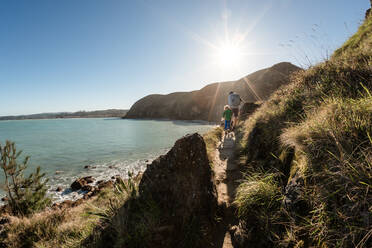 Vater und kleiner Sohn wandern auf einem Bergpfad über dem Meer in Neuseeland - CAVF83298